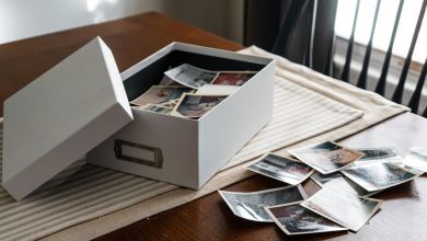 Caixa aberta com fotografias antigas de família sobre uma mesa de madeira, junto à janela