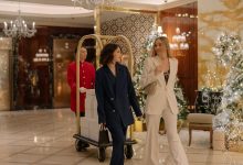 Duas mulheres usando ternos elegantes caminham pelo saguão decorado de um hotel de luxo.