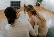 Duas mulheres sentadas em ambiente interno, conversando com empatia e oferecendo apoio uma à outra.