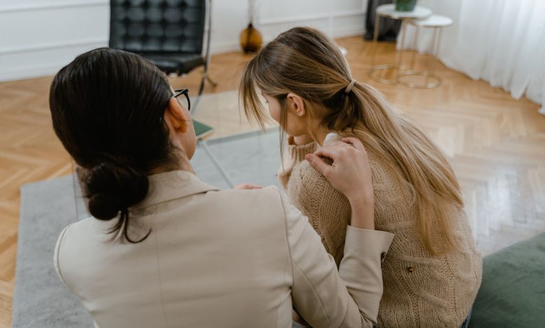 Duas mulheres sentadas em ambiente interno, conversando com empatia e oferecendo apoio uma à outra.